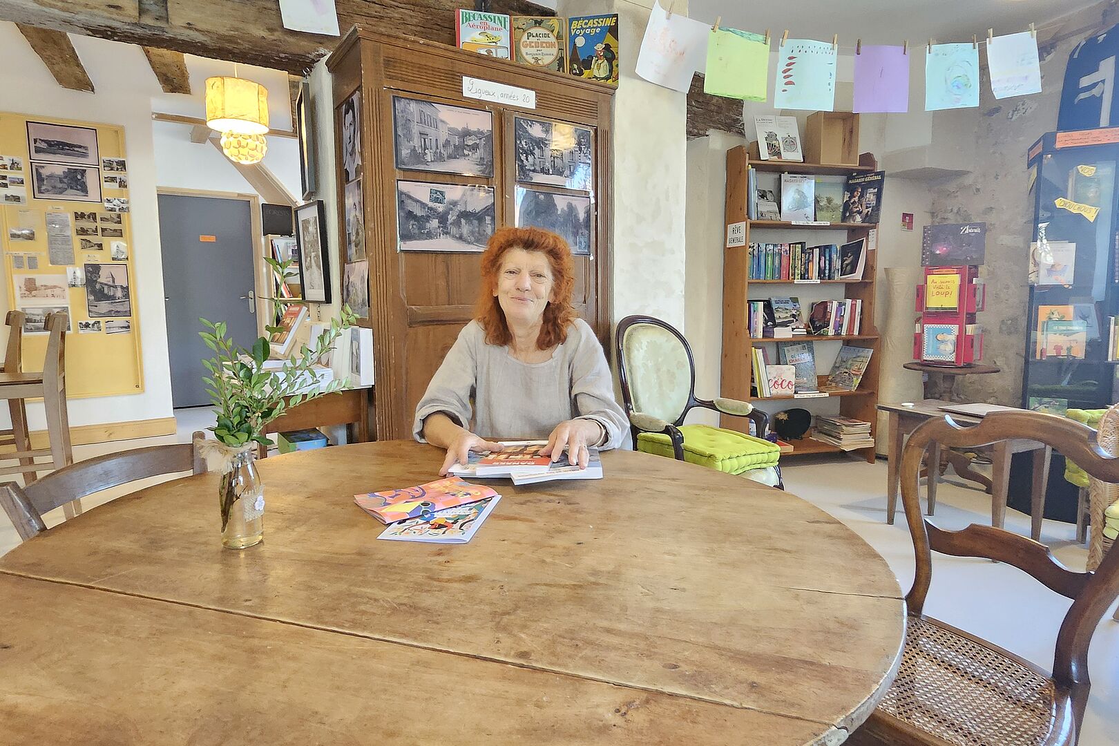 Simone est assise à table. Derrière elle, dans la salle, une armoire est située à côté d'une étagère pleine de livres