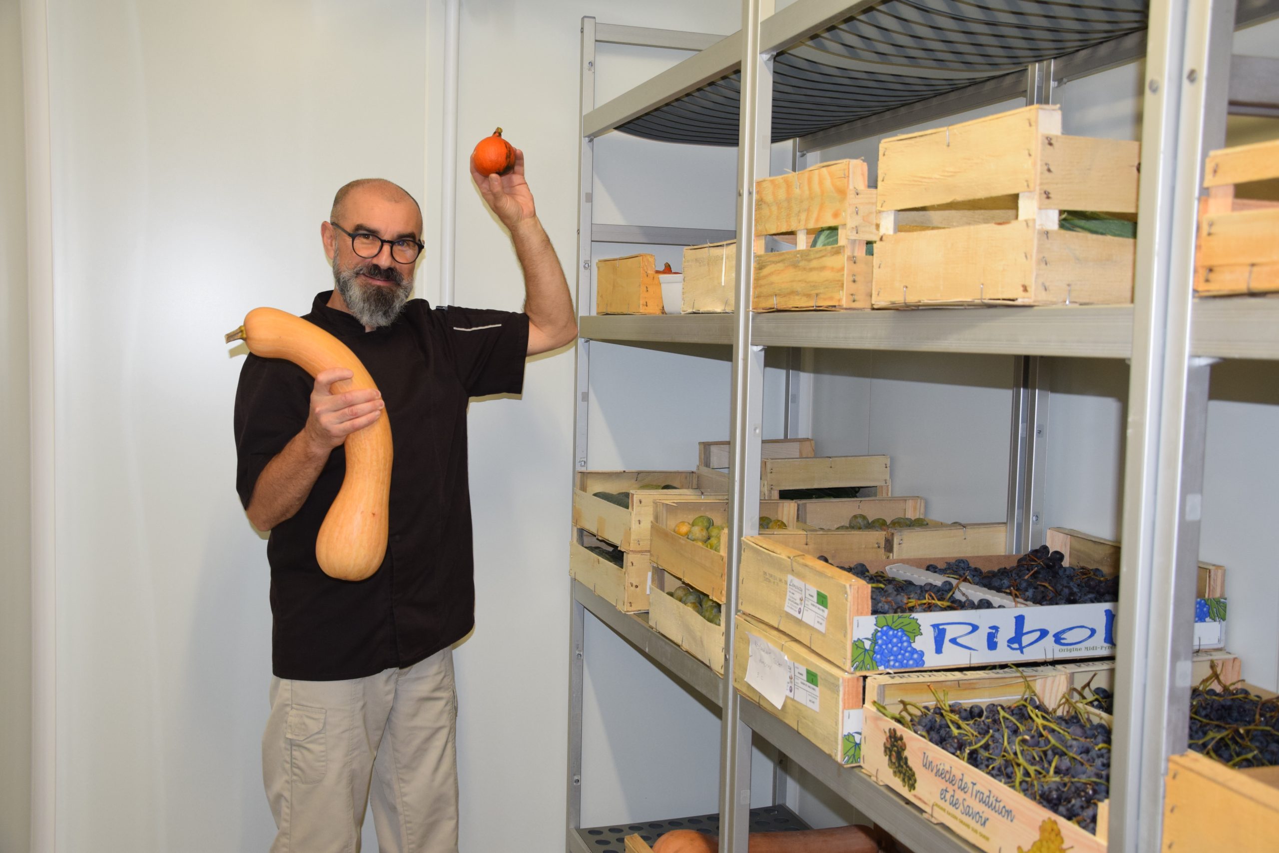 Le chef cuisinier du restaurant scolaire de Champcevinel montre des légumes dans un espace réfrigéré dédié