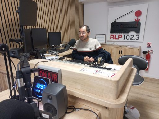 Un homme est assis devant une station de radio. Derrière lui, il y a écrit RLP.