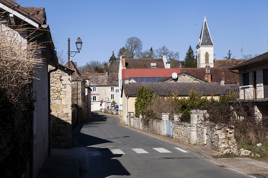 Une rue traverse le village. De chaque côté, des murs, des bâtiments en pierre.