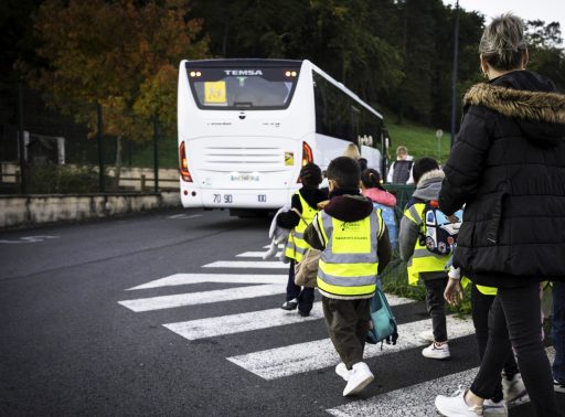 Des enfants de dos portent des brassards fluos inscrits Grand Périgueux. Ils vont prendre un autocar