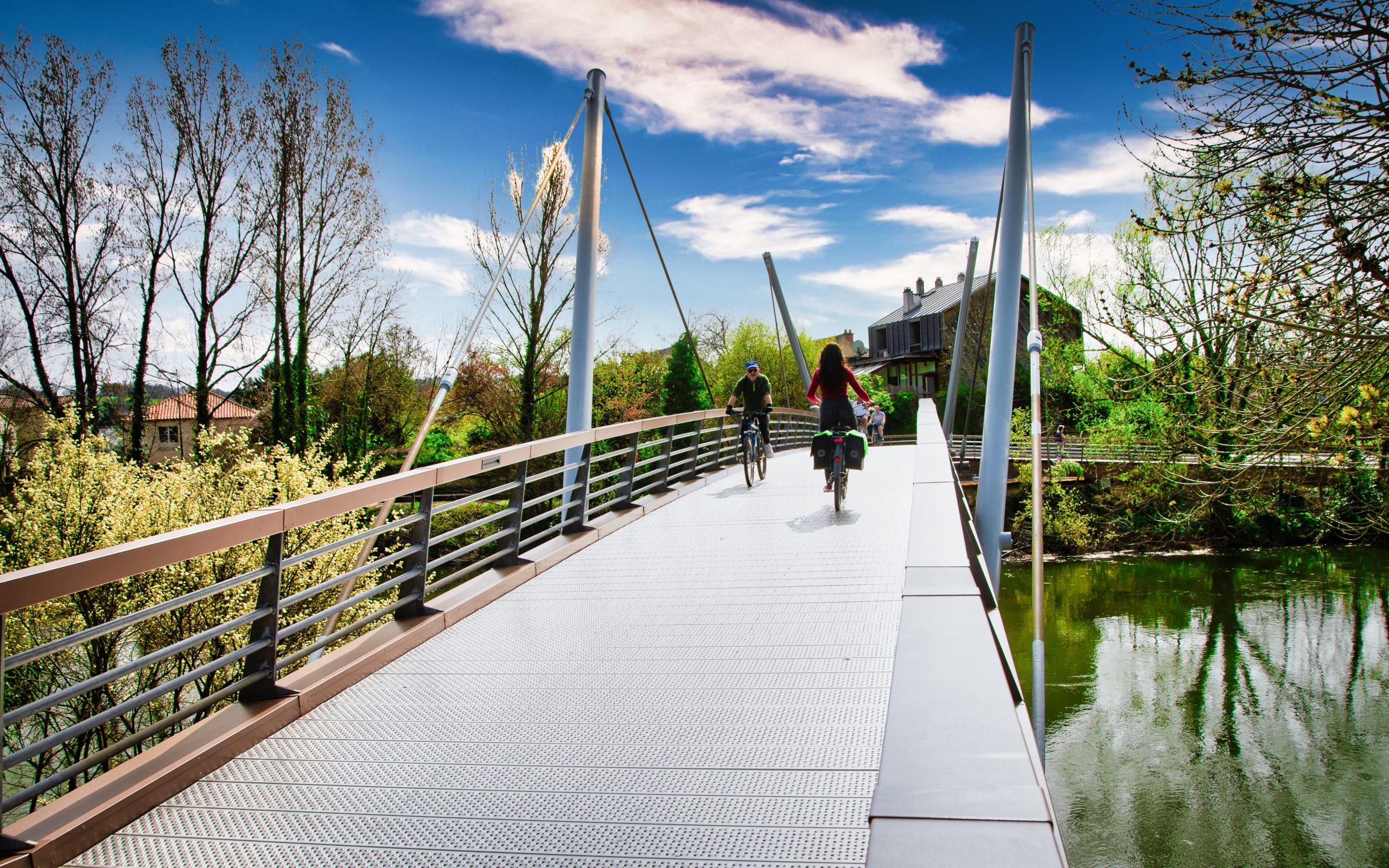 Des personnes sont à vélos et passent par une passerelle pour traverser la rivière