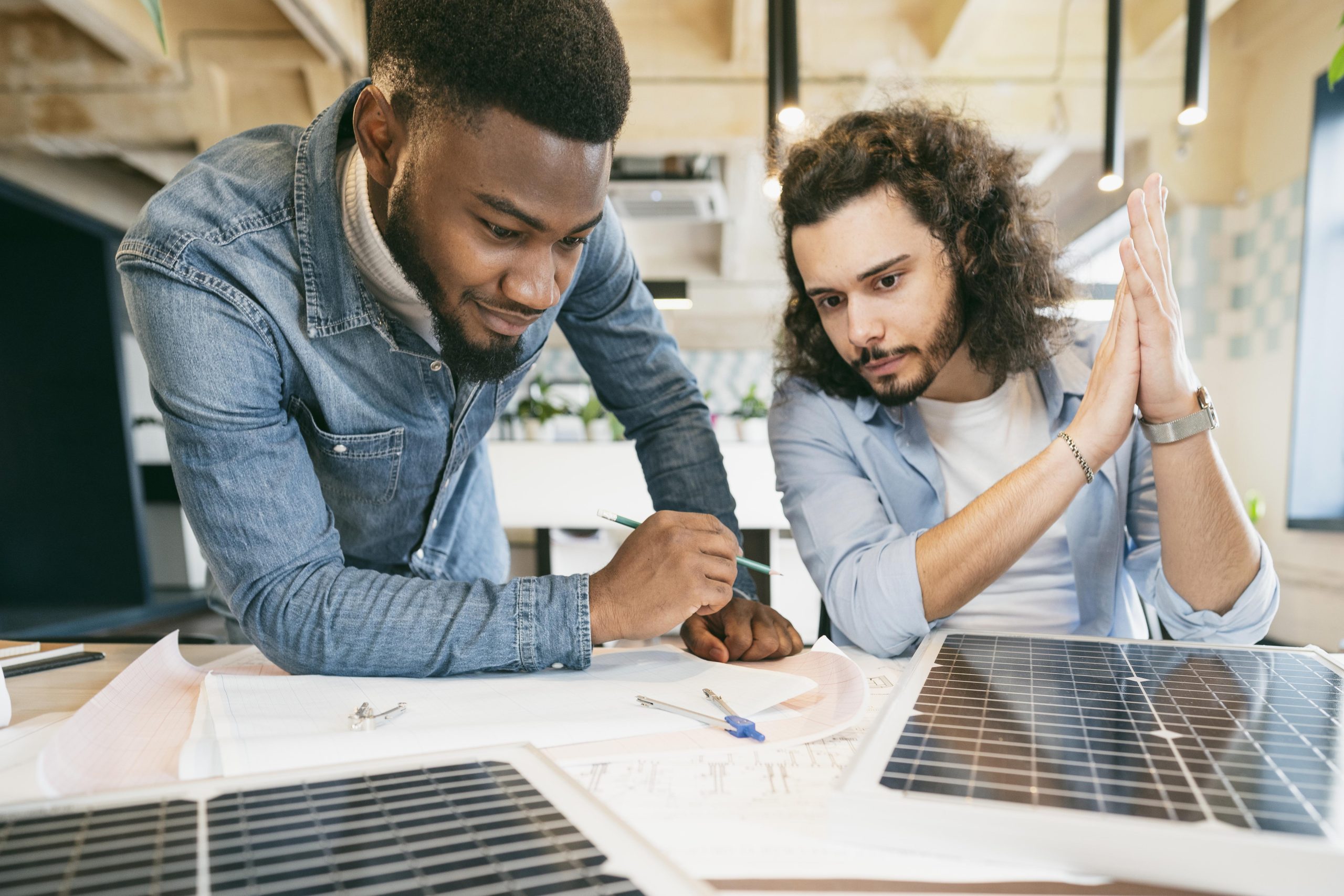 Deux hommes réfléchissent à avec des plans sur une table et des panneaux solaires pour réaliser des économies d'énergie.