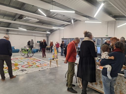 Dans une des vastes halles du Sîlot, le public se renseigne sur les différents stands d'entreprises d'économie sociale et solidaire. D'autres découvrent le monde de l'économie sociale et solidaire à travers un jeu de l'oie géant sur ce thème disposé au sol.