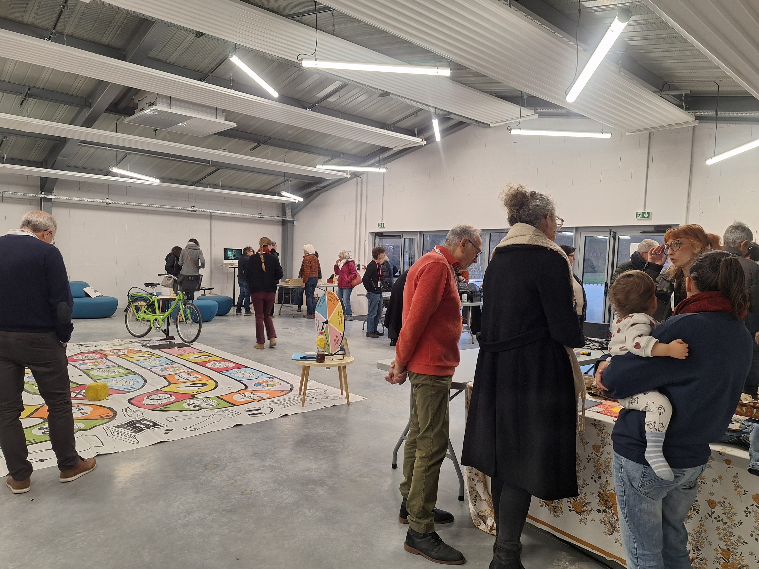 Dans une des vastes halles du Sîlot, le public se renseigne sur les différents stands d'entreprises d'économie sociale et solidaire. D'autres découvrent le monde de l'économie sociale et solidaire à travers un jeu de l'oie géant sur ce thème disposé au sol.