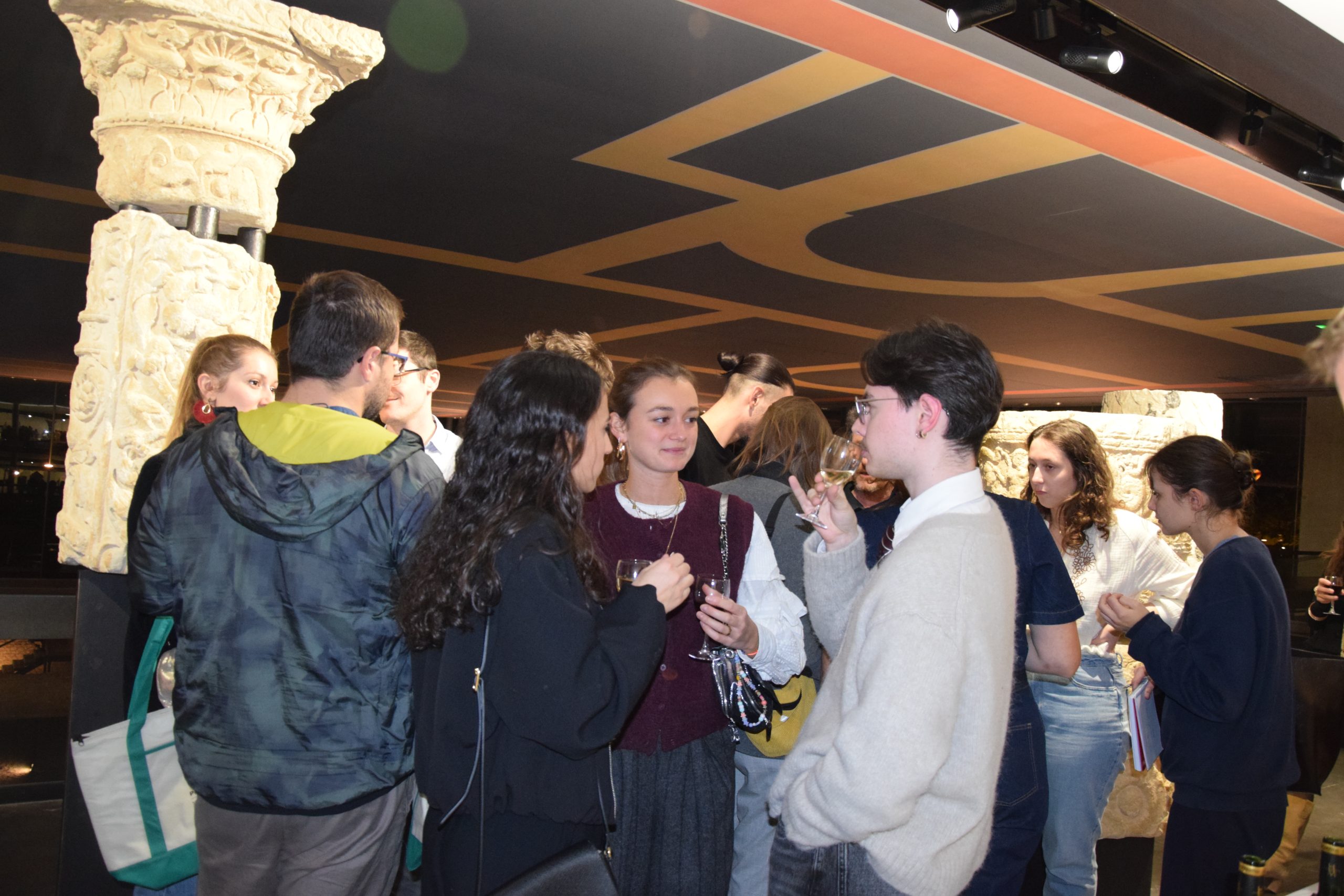 Des jeunes trinquent. Ils sont installés au musée Vesunna à Périgueux,. il est possible d'y apercevoir une colonne en pierres et le plafond du musée conçu par Jean Nouvel.