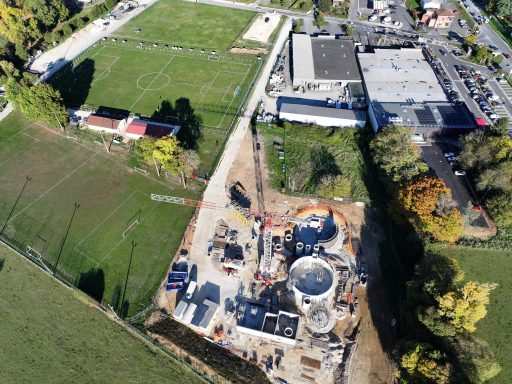 Photo prise du ciel montrant une station d'épuration en construction au cœur d'une zone de vergt comprenant des commerces et des terrains de football.