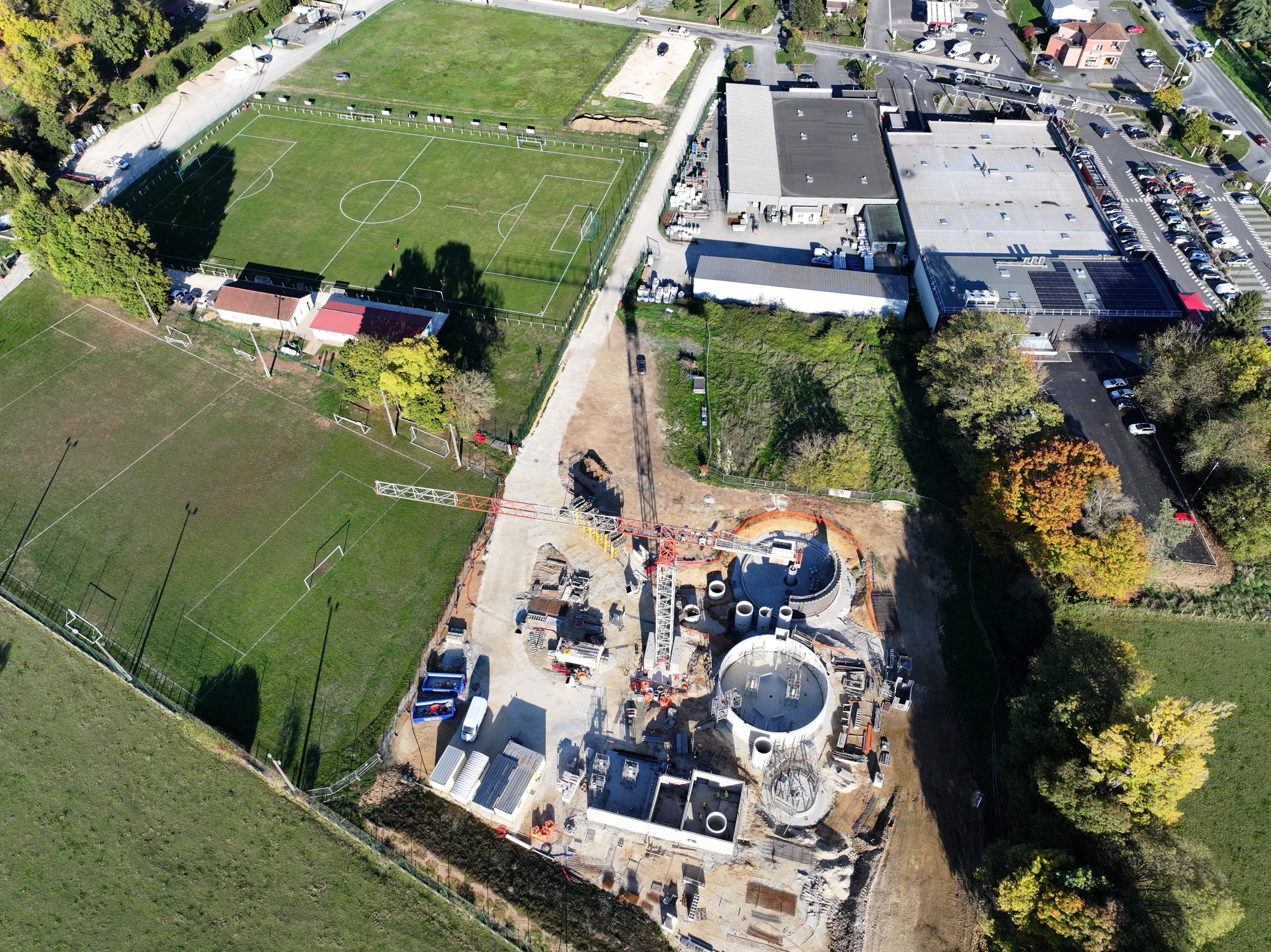 Photo prise du ciel montrant une station d'épuration en construction au cœur d'une zone de vergt comprenant des commerces et des terrains de football.