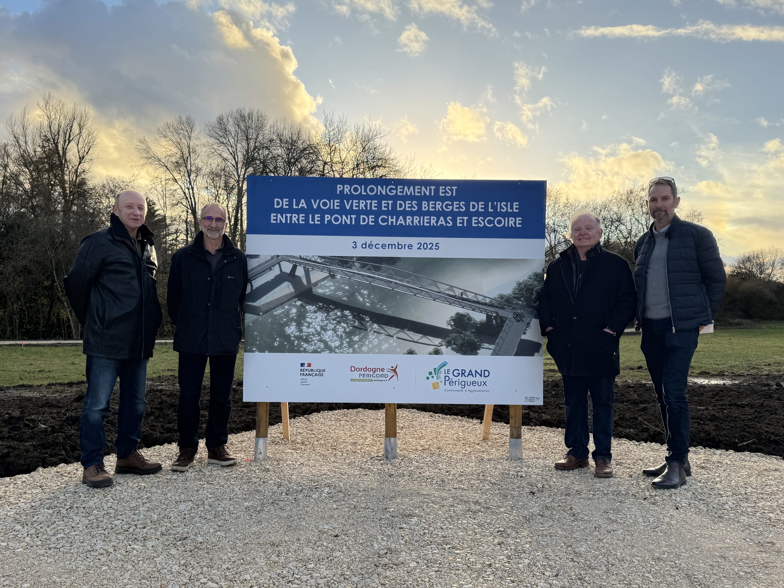 Le maire d'Antonne-et-Trigonant Daniel Le Mao et son conseiller municipale Jean-Luc Planche posent aux côtés d'Olivier Georgiadès vice-président du Grand Périgueux en charge des mobilités durables et de Joël Laguionie maire d'Escoire autour du panneau de chantier de l'extension de la voie verte. Ce panneau montre une photo de la future passerelle qui enjambera la rivière.