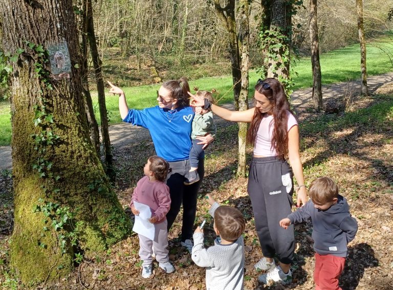 Les enfants accompagnés par deux assistantes maternelles découvrent la nature et regardent de près les arbres.