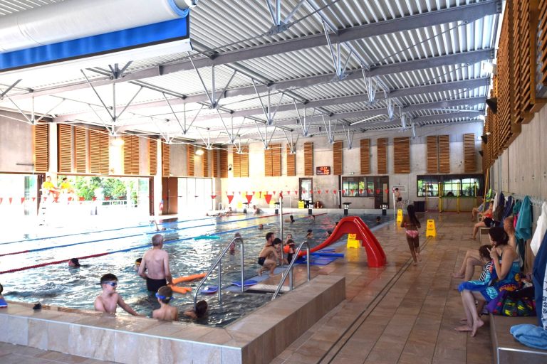 De nombreuses personnes nagent et sont dans l'eau d'une piscine. Il s'agit de celle de Niversac, reconnaissable sur le côté avec le bois.