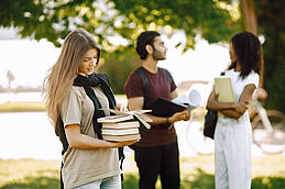 Three international students standing in a park and holding a bo